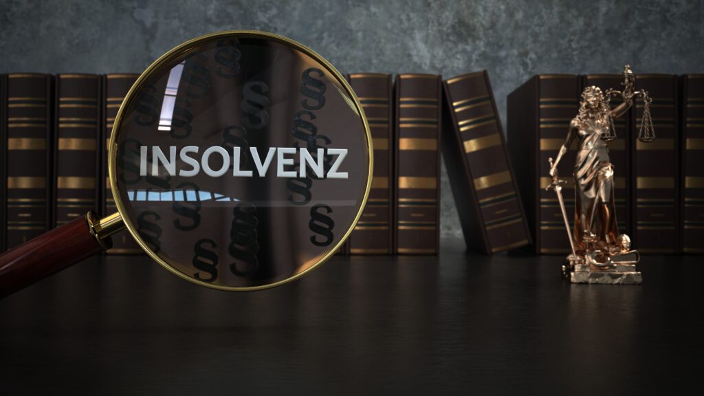 Lupe mit Schriftzug ‚Insolvenz‘ vor Gesetzesbüchern und Justitia-Figur – Symbolbild für Insolvenzrecht.